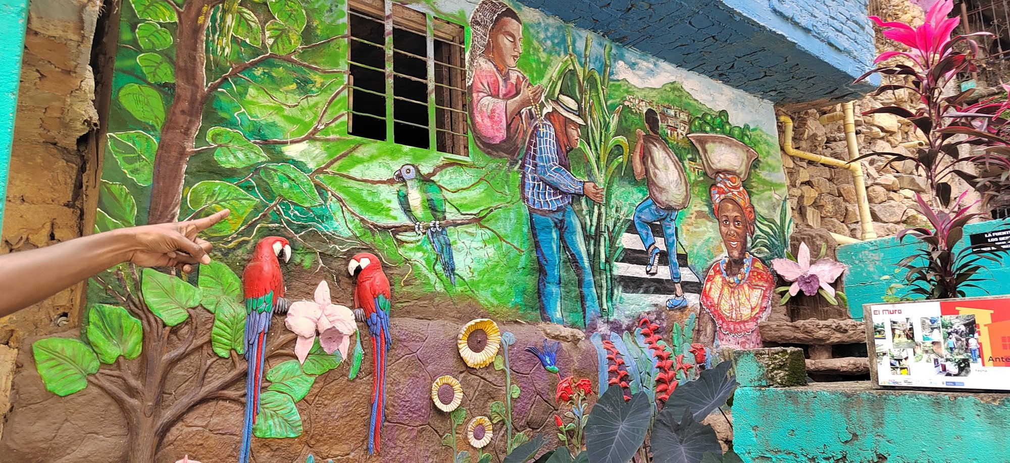 A community mural in Cali, Colombia, depicting Afro-Colombian figures, agricultural work, native birds and lush vegetation in vivid greens, reds and blues.